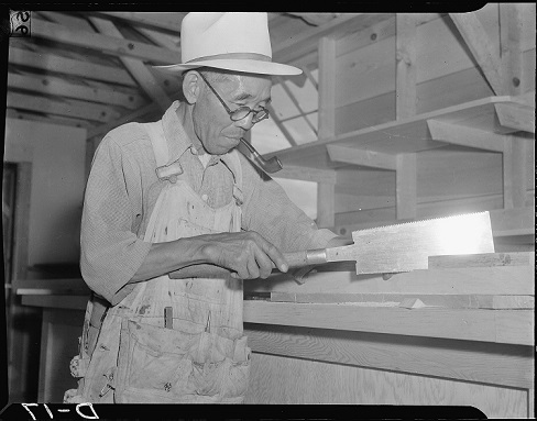 Japanese American Incarceree working as cabinet worker, sawing on the interior construction of general store Number 2 at this War Relocation Authority center for evacuees of Japanese descent